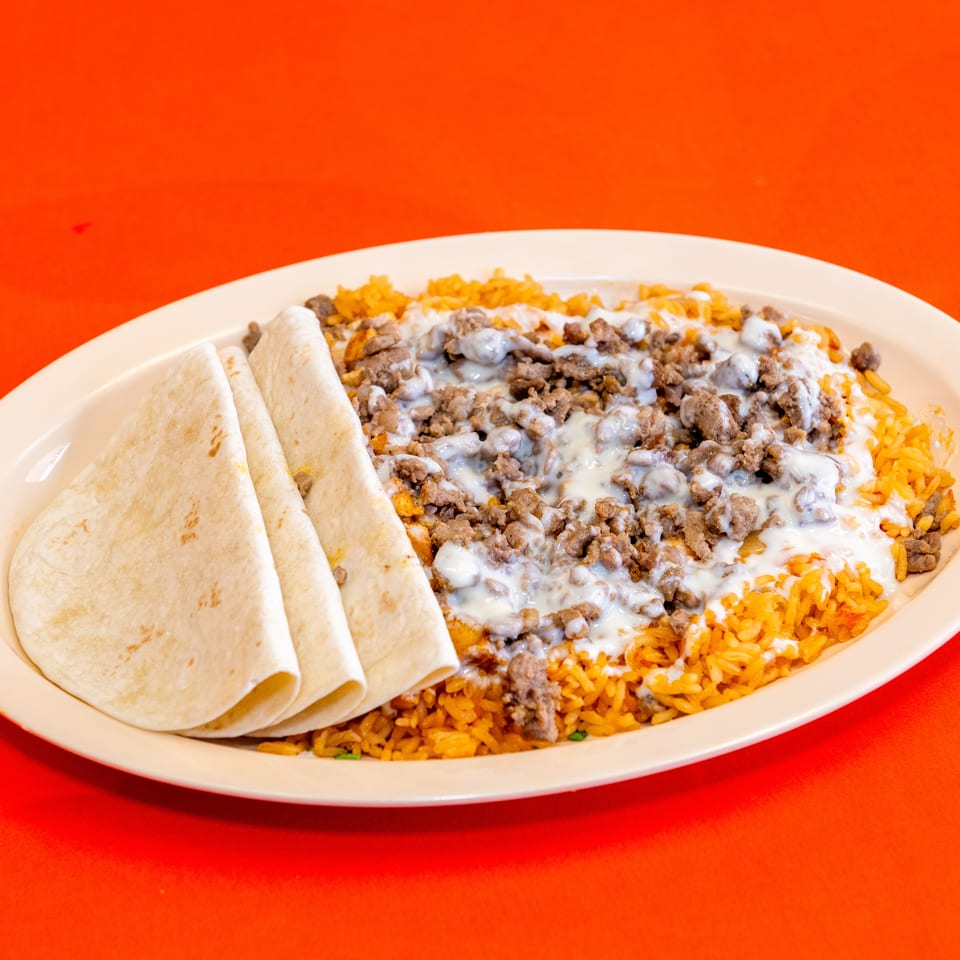 Plate of rolled flour tortillas, seasoned rice, chopped beef, and melted white cheese on a bright red table.