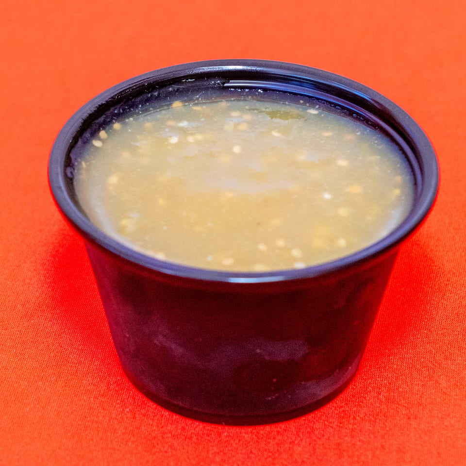Bowl of pale, creamy soup with small grains or pieces, served in a dark ceramic bowl on a bright red tablecloth.