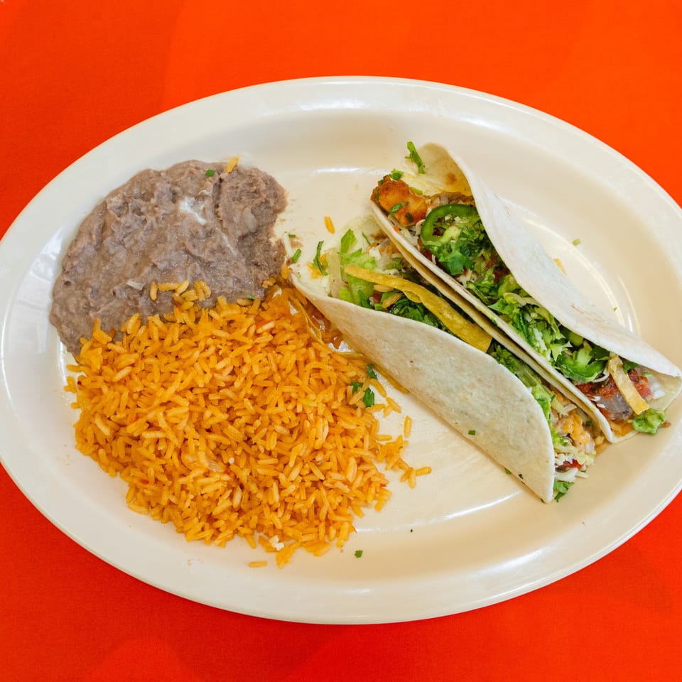 Two tacos served with rice and refried beans.