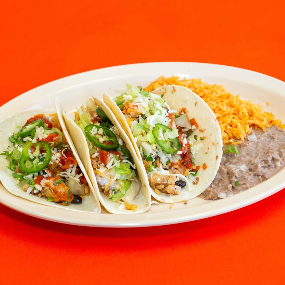 Three soft tacos topped with lettuce, cheese, salsa, and jalapeños, served with Mexican rice and refried beans.