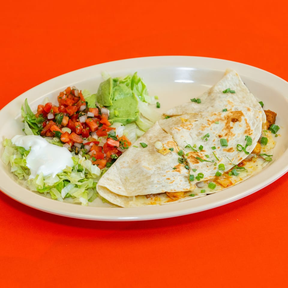 Cheese quesadillas with lettuce, pico de gallo, sour cream, and guacamole served on a white platter.