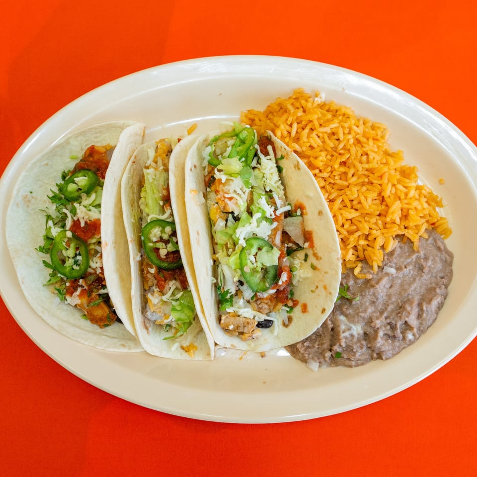 Three tacos with rice and beans.