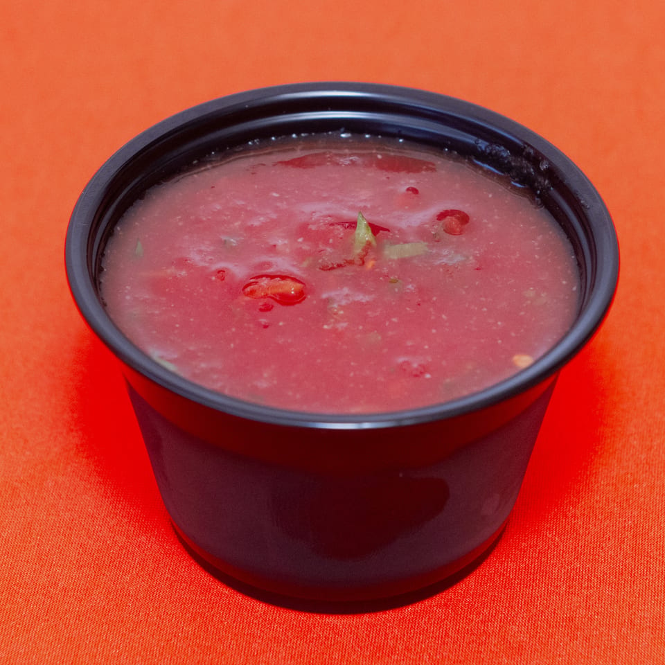 Black bowl of pink soup garnished with sliced vegetables on an orange tablecloth.